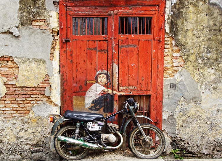 Oldtimer-Motorrad vor einer verwitterten Holztür mit Wandmalerei an einer alten Ziegelwand im urbanen Stil.
