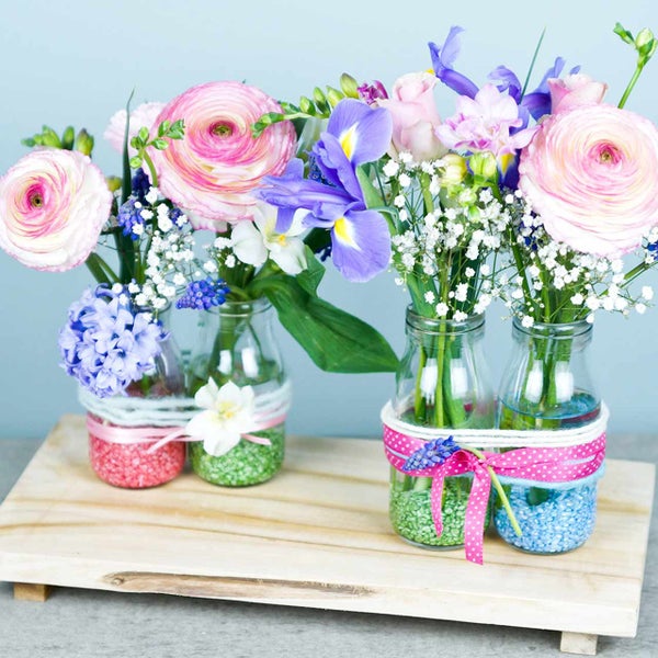 Frühlingshaftes Blumenarrangement in kleinen Glasflaschen auf einem Holztablett mit Ranunkeln und Iris.