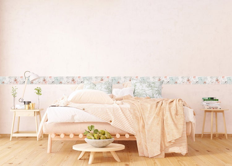 Helles Schlafzimmer mit einer floralen Tapetenbordüre an einer neutralen Wand hinter einem Bett mit hellen Textilien und Holzmöbeln.