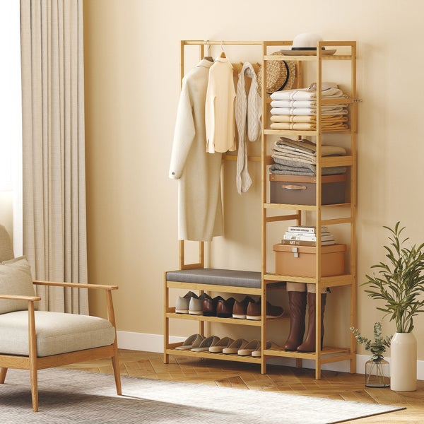 Garderobenständer aus Holz mit Schuhregal, Sitzbank und Seitenregal in hellem Raum mit Sessel und Pflanze.