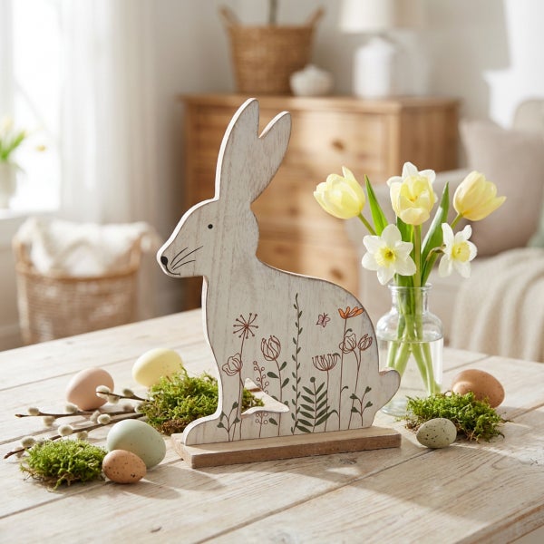 Osterdekoration aus Holz in Hasenform mit floralem Muster auf einem Holztisch mit Frühlingsblumen und Ostereiern.