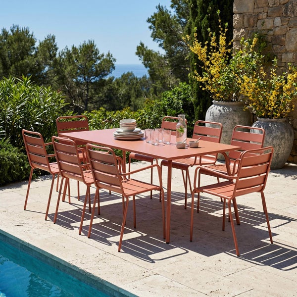 Moderner Garten-Essbereich mit rechteckigem Metalltisch und acht Stühlen in Terrakotta auf einer hellen Steinterrasse neben einem Pool.