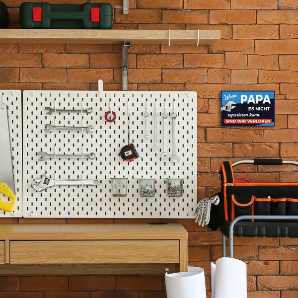 Blechschild mit Spruch Wenn Papa es nicht reparieren kann sind wir verloren an Ziegelwand in organisierter Werkstatt neben Lochwand mit Werkzeug.