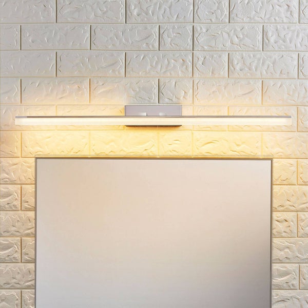 Moderne, lineare LED-Spiegelleuchte über einem Wandspiegel an einer strukturierten Mauerwand. Warmweißes Licht.