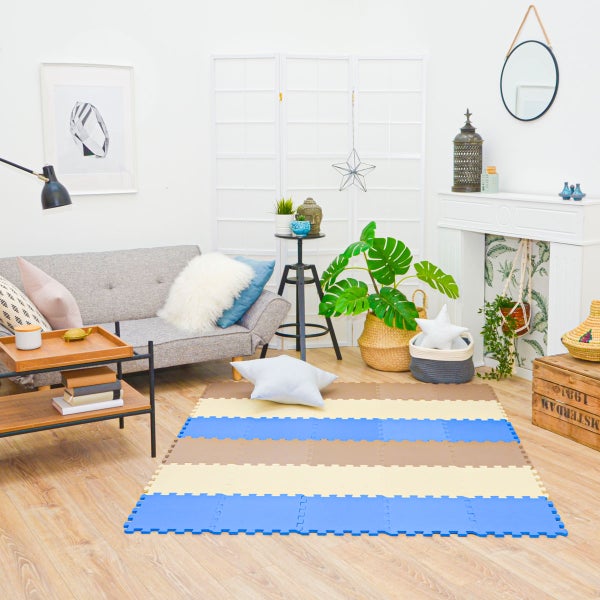 Hell eingerichtetes Wohnzimmer mit grauem Sofa, Pflanzen und einer gestreiften Schaumstoffmatte in Blau, Beige und Braun auf Laminatboden.