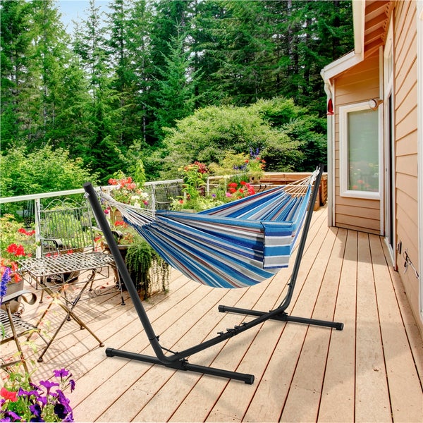 Gestreifte Hängematte mit Metallgestell auf einer Holzterrasse vor üppigem Grün