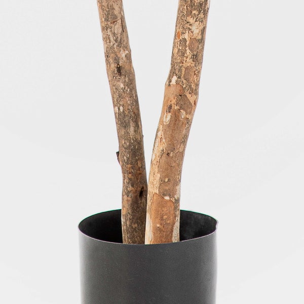 Nahaufnahme von zwei strukturierten Holzstämmen einer Kunstpflanze in einem schwarzen Topf.