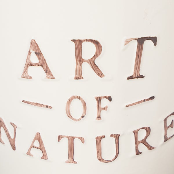 Geprägter Schriftzug Art of Nature mit Pinselstrich-Effekt.