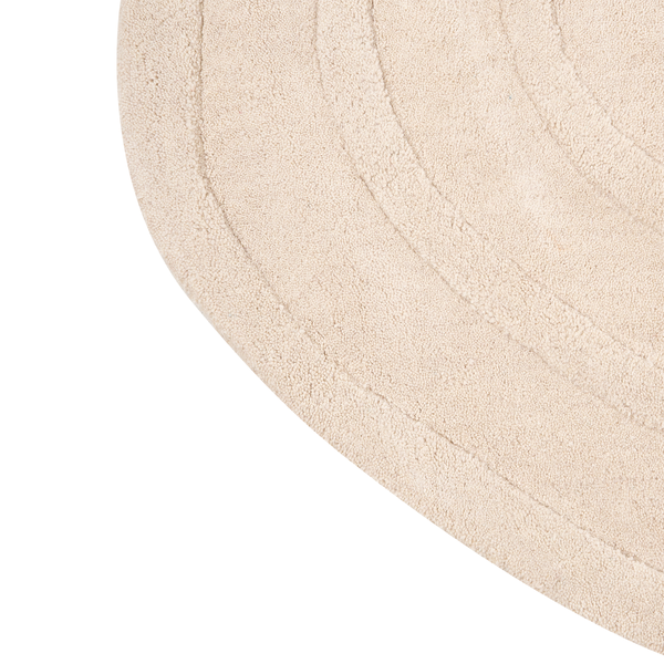 Detail eines runden, beigen Teppichs mit konzentrischen Linien und weicher Textur.