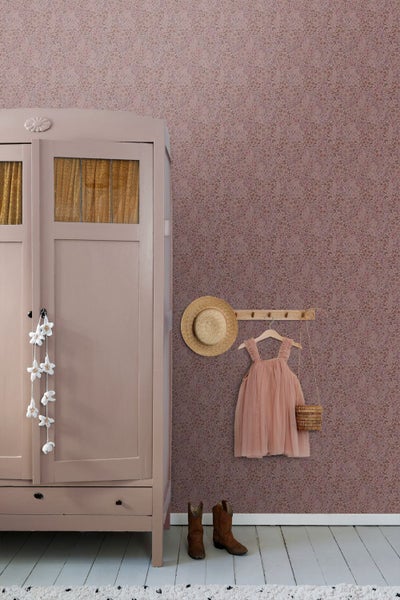Ein gemütlicher Raum mit floraler Vliestapete, einem vintage Holzschrank, einer Hakenleiste mit Kleid und Hut sowie Lederstiefeln auf dem Boden.
