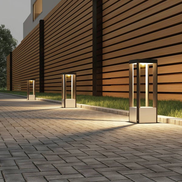 Moderne Wegeleuchten in quadratischem Design mit warmweißem Licht an einem gepflasterten Gartenweg vor einem Holzzaun.