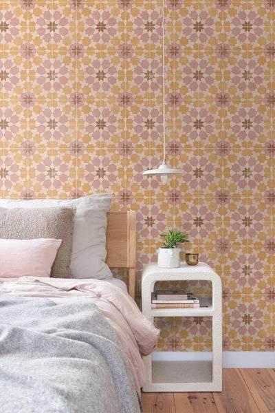 Helles Schlafzimmer mit geometrischer Tapete in Fliesenoptik, Bett mit Holz-Kopfteil und weißem Beistelltisch.