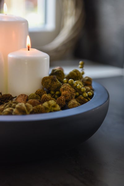 Dekoschale mit weißen Stumpenkerzen und natürlichem Streumaterial wie Moos, Zapfen und Beeren.