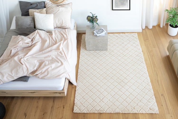 Helles Schlafzimmer mit Holzbett, strukturierter Rauten Teppich, Nachttisch aus Stein und Zimmerpflanze in modernem Design.