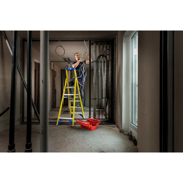 Ein Mann arbeitet auf einer gelben Stufenleiter in einem Raum im Rohbau und verlegt Kabel.