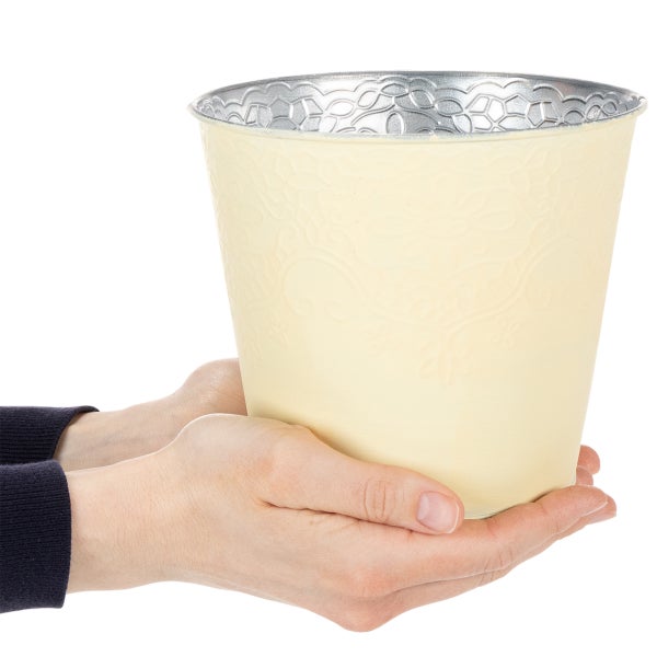 Cremefarbener Übertopf aus Metall mit Reliefmuster in den Händen gehalten.