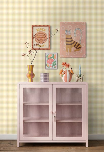 Gelb-weiß karierte Tapete hinter einer rosa Vitrine mit bunter Dekoration und gerahmter Kunst.