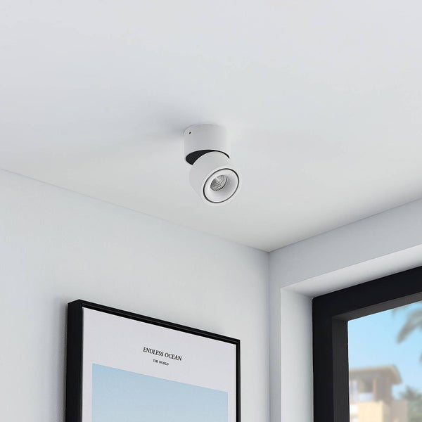 Moderner weißer Deckenstrahler in zylindrischer Form, verstellbar, montiert an einer weißen Decke über einem Bild in einem hellen Raum.