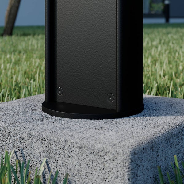 Detailansicht eines schwarzen Pfostenfußes aus strukturiertem Metall, montiert auf einem grauen Betonsockel im Garten.