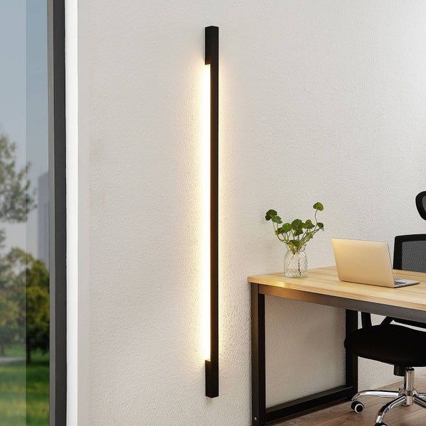 Schwarze LED-Wandleuchte in minimalistischem Design in einem hellen Büro neben einem Schreibtisch mit Laptop.