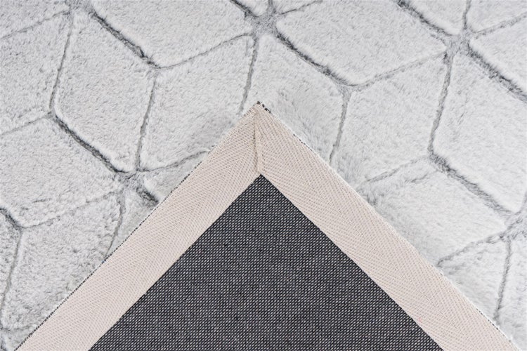 Nahaufnahme eines Teppichs mit geometrischem Rautenmuster und weicher Struktur, eine umgeklappte Ecke zeigt die Rückseite.