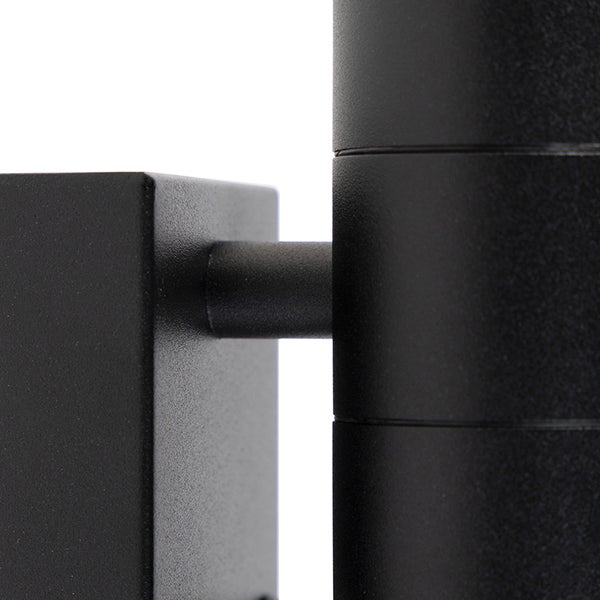 Nahaufnahme einer schwarzen Wandleuchte aus Metall, Verbindung zwischen rechteckiger Halterung und zylindrischem Leuchtenkopf.