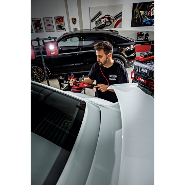 Ein Handwerker poliert mit einem Flex Akku Exzenterschleifer das Dach eines weißen Autos in einer professionellen Werkstatt.