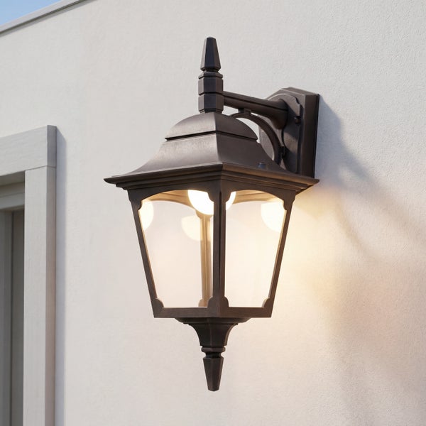 Klassische, laternenförmige Außenwandleuchte aus Metall und Glas, montiert an einer Hauswand und eingeschaltet mit warmem Licht.