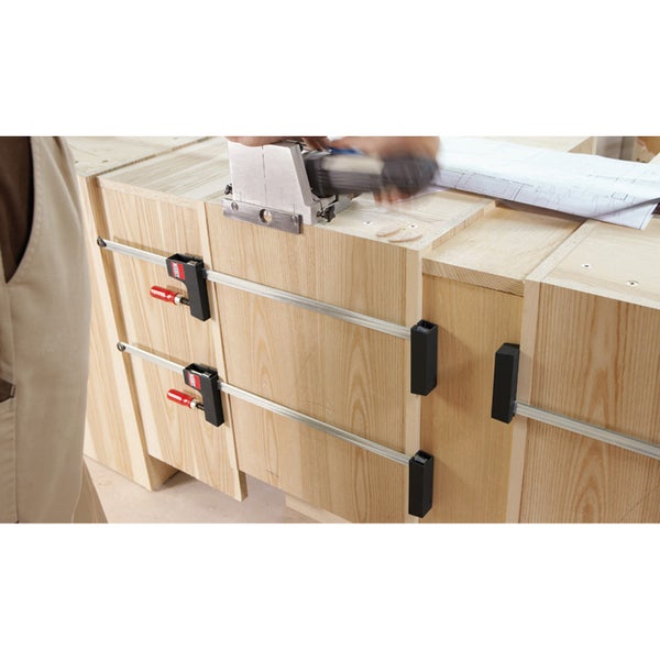 Bessey Korpuszwingen fixieren Holzplatten beim Möbelbau, während eine Person eine Flachdübelfräse zur Bearbeitung verwendet.