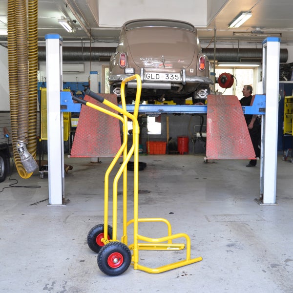 Gelber Reifenwagen in einer Werkstatt mit angehobenem Oldtimer.