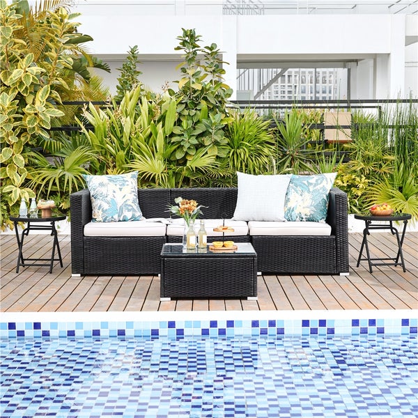 Modernes Garten-Lounge-Set aus schwarzem Polyrattan mit Sofa, Tisch und Beistelltischen auf einer hellen Holzterrasse am Pool.