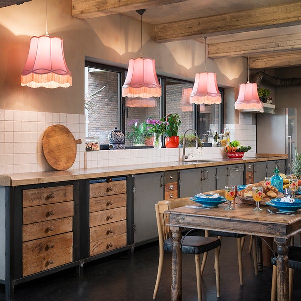 Rustikale Küche mit langer Arbeitsplatte, Holzschränken und vier rosa Stoff-Pendelleuchten mit Fransen über dem Essbereich.