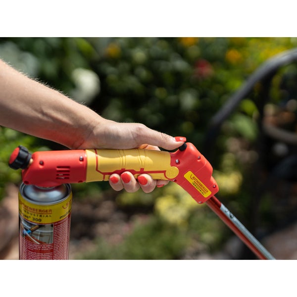 Eine Hand hält einen Rothenberger Industrial Unkrautbrenner mit angeschlossener Gaskartusche in einem Garten.