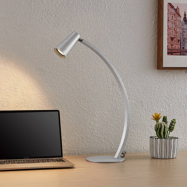 Moderne LED-Schreibtischlampe aus Metall mit gebogenem Arm auf einem Schreibtisch neben einem Laptop.