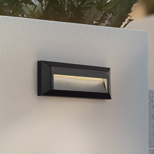 Moderne rechteckige Außenwandleuchte in Schwarz an einer strukturierten Wand mit warmweißem Lichtaustritt nach unten.