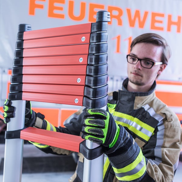 Feuerwehrmann hält eine kompakte Teleskopleiter mit orangefarbenen Sprossen und Markierungen für verschiedene Höhenmeter.