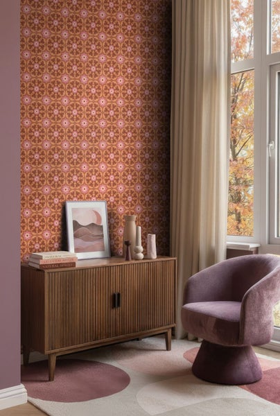Vliestapete mit retro Blumenmuster in einem Wohnzimmer mit Holz-Sideboard, violettem Sessel und herbstlichem Ausblick.