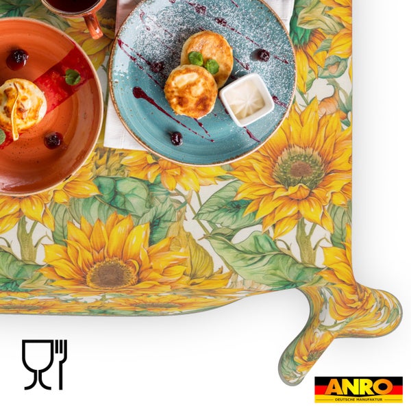 Abwaschbare Tischdecke mit Sonnenblumenmuster und Blättern, gedeckter Tisch mit Tellern und Speisen. ANRO Deutsche Manufaktur Logo. Lebensmittelunbedenklich.
