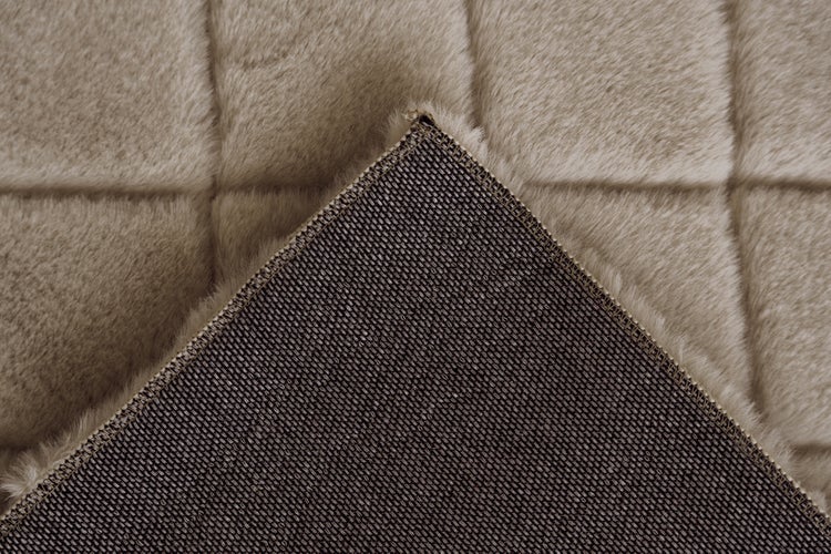 Nahaufnahme eines plüschigen Kunstfellteppichs mit Steppmuster und einer gewebten, rutschfesten Rückseite.