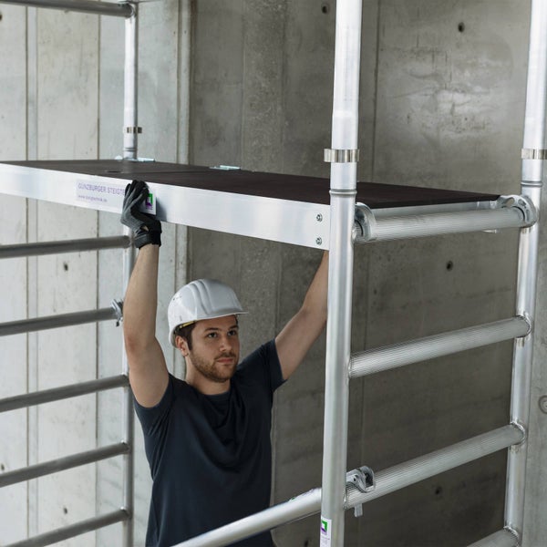 Mann montiert ein Gerüst mit einer Arbeitsplattform aus Aluminium und Holz.