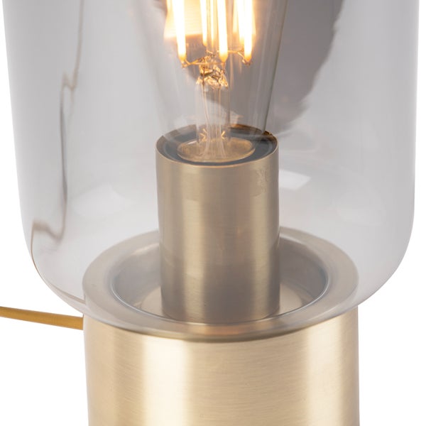 Nahaufnahme einer Tischleuchte mit Schirm aus klarem Glas, Fassung aus gebürstetem Metall und LED Leuchtmittel.