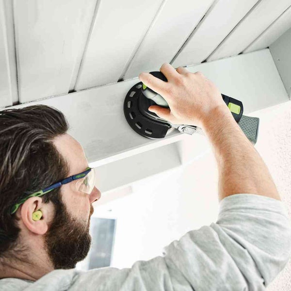 Mann schleift mit einem Rotationsschleifer eine Holzoberfläche.