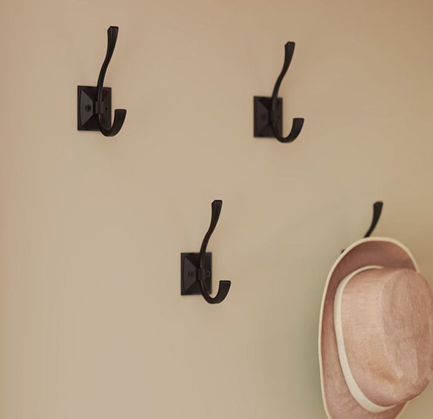 Drei schwarze Kleiderhaken an einer Wand, einer davon mit Hut