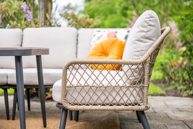 Garten-Lounge-Sofa mit Armlehne aus Seilgeflecht, hellen Kissen und Dekokissen auf einer Terrasse im Garten.