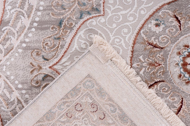 Nahaufnahme eines Teppichs mit ornamentalem Paisley-Muster und umgeschlagener Ecke, die die gewebte Rückseite und Fransen zeigt.