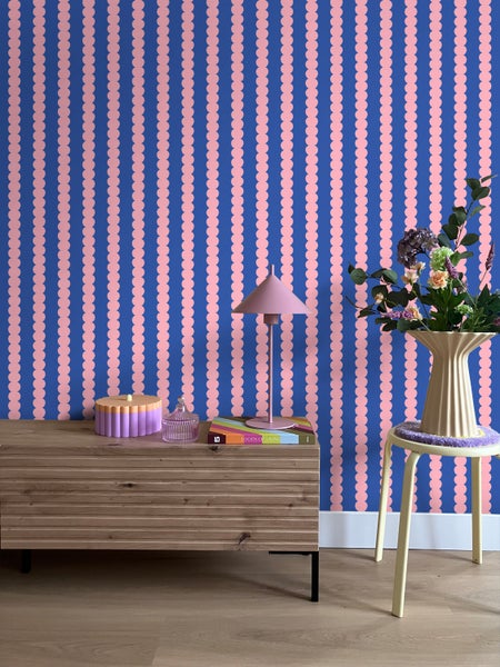 Zimmer mit Kommode, Hocker, Tischleuchte und Tapete mit Streifenmuster