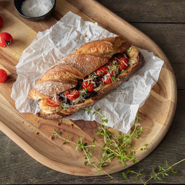 Baguette mit Tomaten, Oliven und Käse auf einem Holzbrett