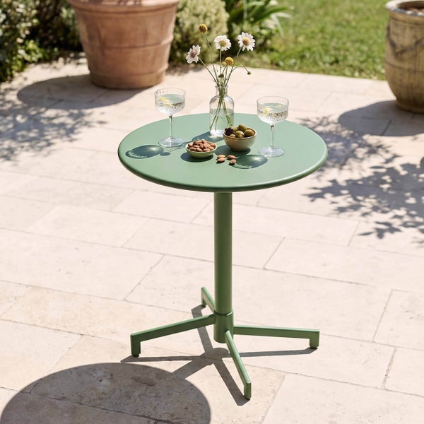 Runder Bistro-Tisch aus Metall auf einer hellen Terrasse mit Gläsern, einer Blumenvase und Snacks.