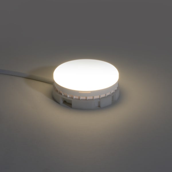 Runde LED Möbelleuchte aus Kunststoff, eingeschaltet mit warmweißem Licht und Anschlusskabel.