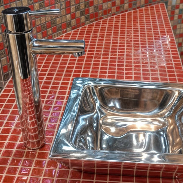 Moderne Waschtischarmatur mit einem quadratischen Waschbecken aus Metall auf einer Ablage mit Mosaikfliesen im Badezimmer.